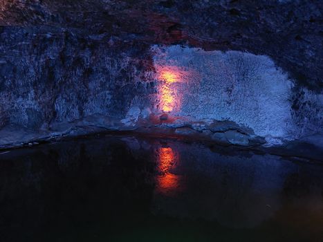 A stunning cave scene featuring red illumination reflecting on dark water, creating a dramatic effect.