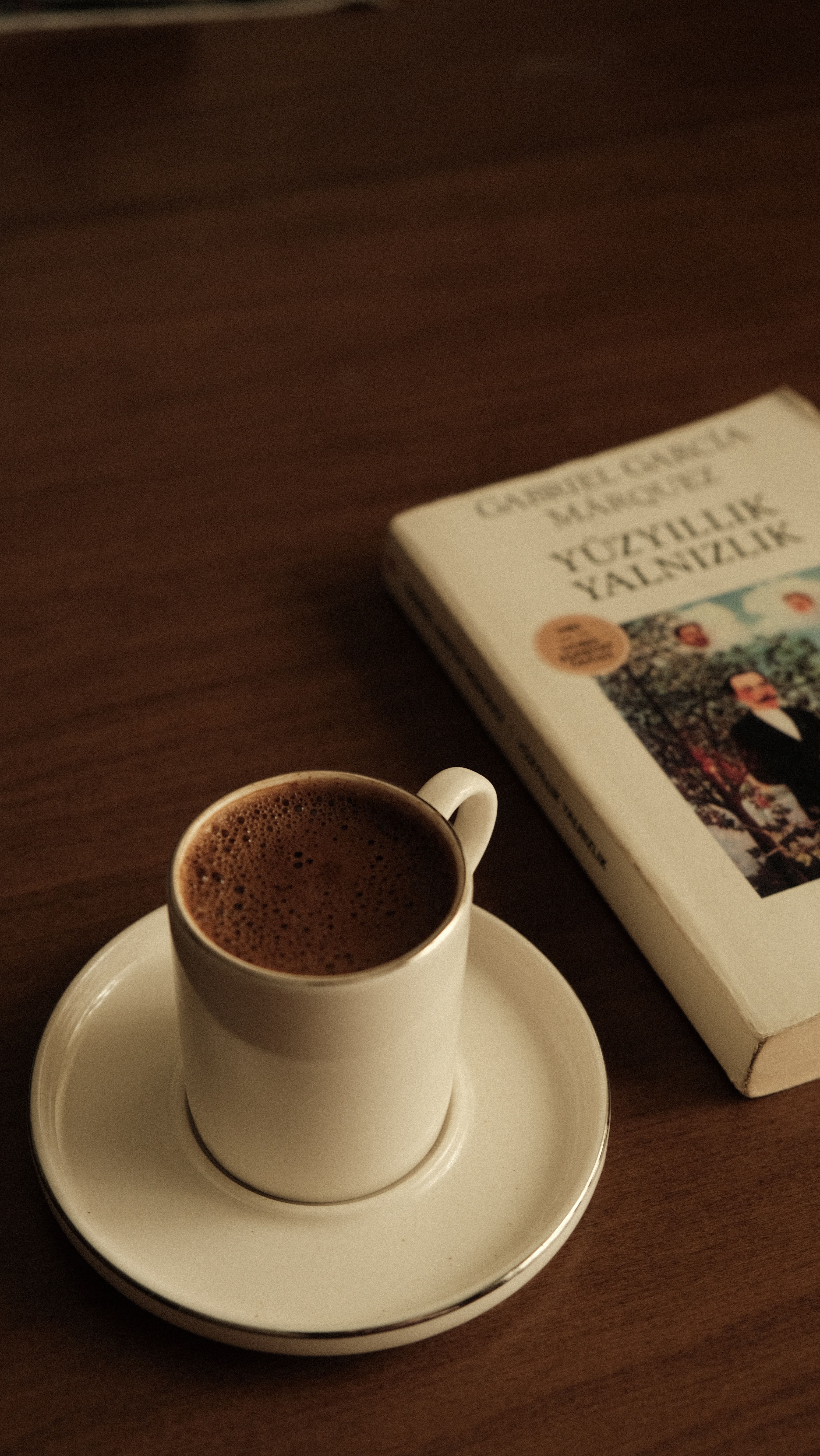 Warm cup of coffee resting next to a book on a wooden table, perfect for a tranquil moment.