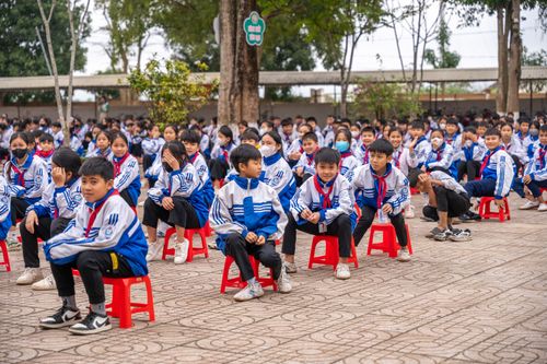 Free Students in uniform gathered for an outdoor school ceremony, sitting on red stools. Stock Photo