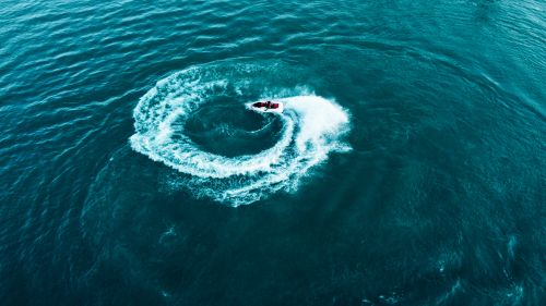 Free A jet ski creates a dynamic circular wake on the ocean surface, captured from above. Stock Photo