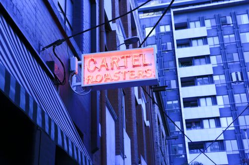 Free A vibrant neon sign for 'Cartel Roasters' in a Melbourne alleyway, showcasing urban cityscape charm. Stock Photo