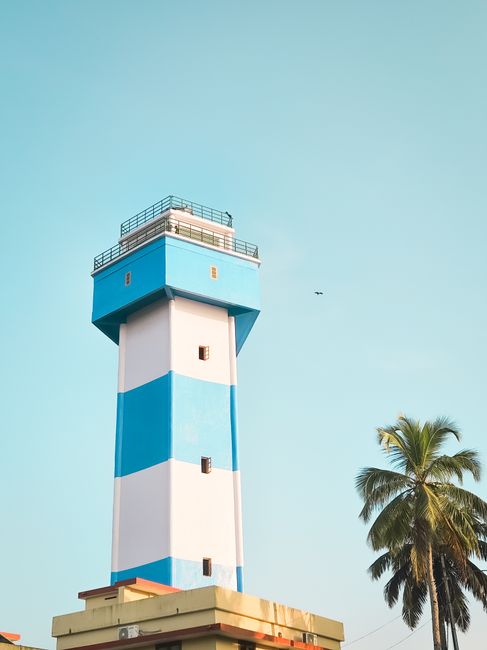 Valiyazhikkal Lighthouse in India with a vibrant blue sky and palm tree.