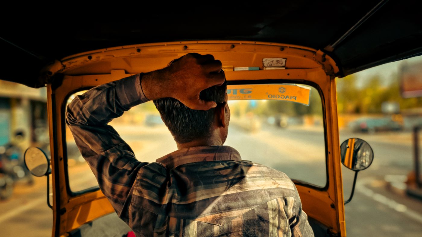 An auto rickshaw driver at work, seen from the back seat