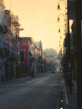 Charming street in Puebla, Mexico at sunset, featuring colorful facades and vintage streetlights.