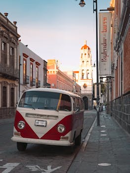 A classic red and white Volkswagen van parked on a picturesque street in Puebla, Mexico, with historic buildings.