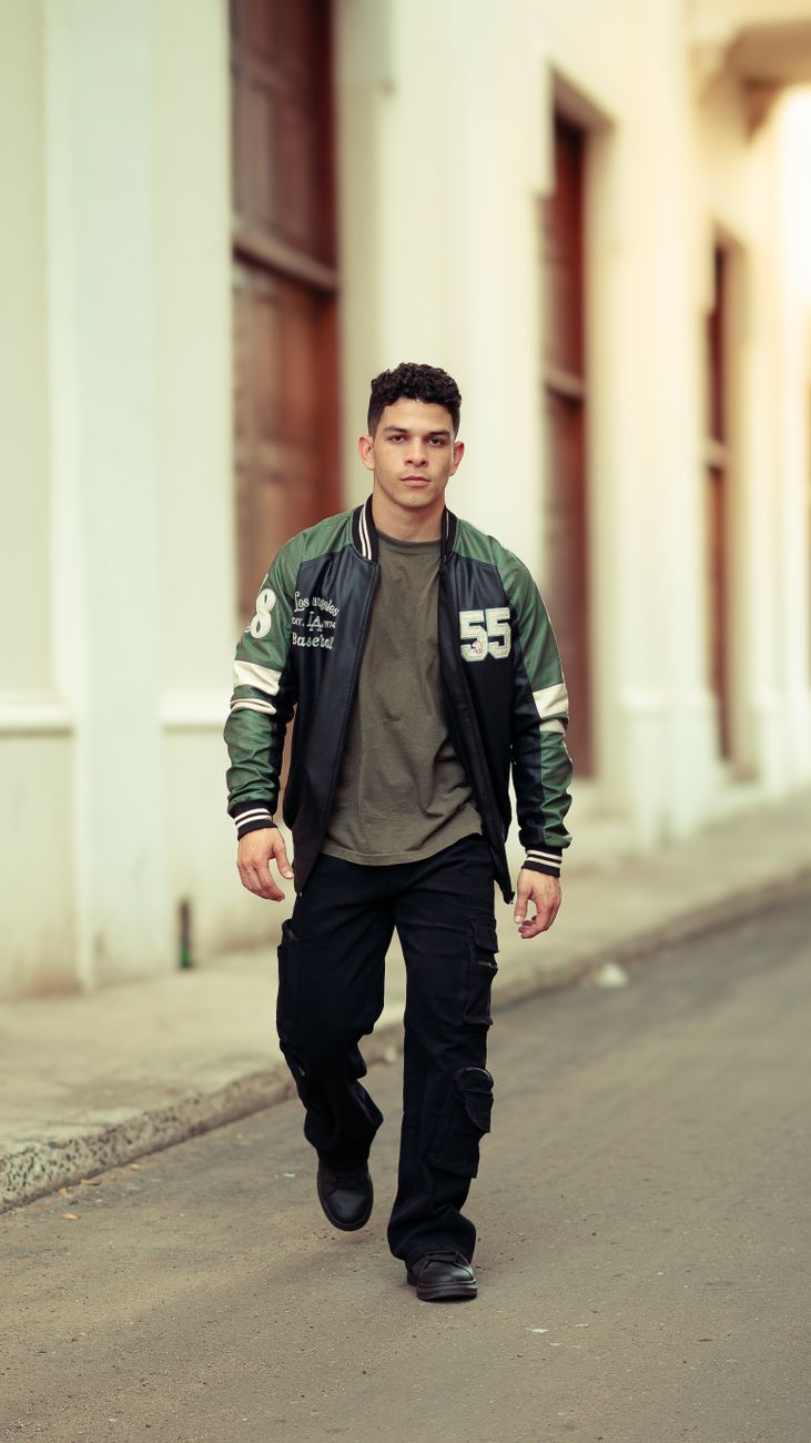 Young man in varsity jacket strolling on a city street, showcasing casual street fashion.