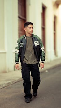 Stylish young man in a varsity jacket and black cargo pants walking on urban street.