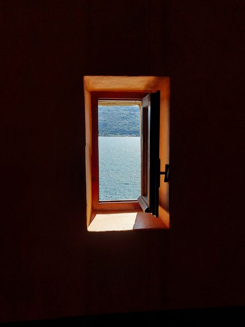 Free Serene view of Lago Maggiore through an open window, creating a peaceful indoor scene. Stock Photo