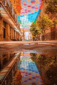 Vibrant street scene with colorful canopy in Guadalajara, Mexico reflecting in a puddle.
