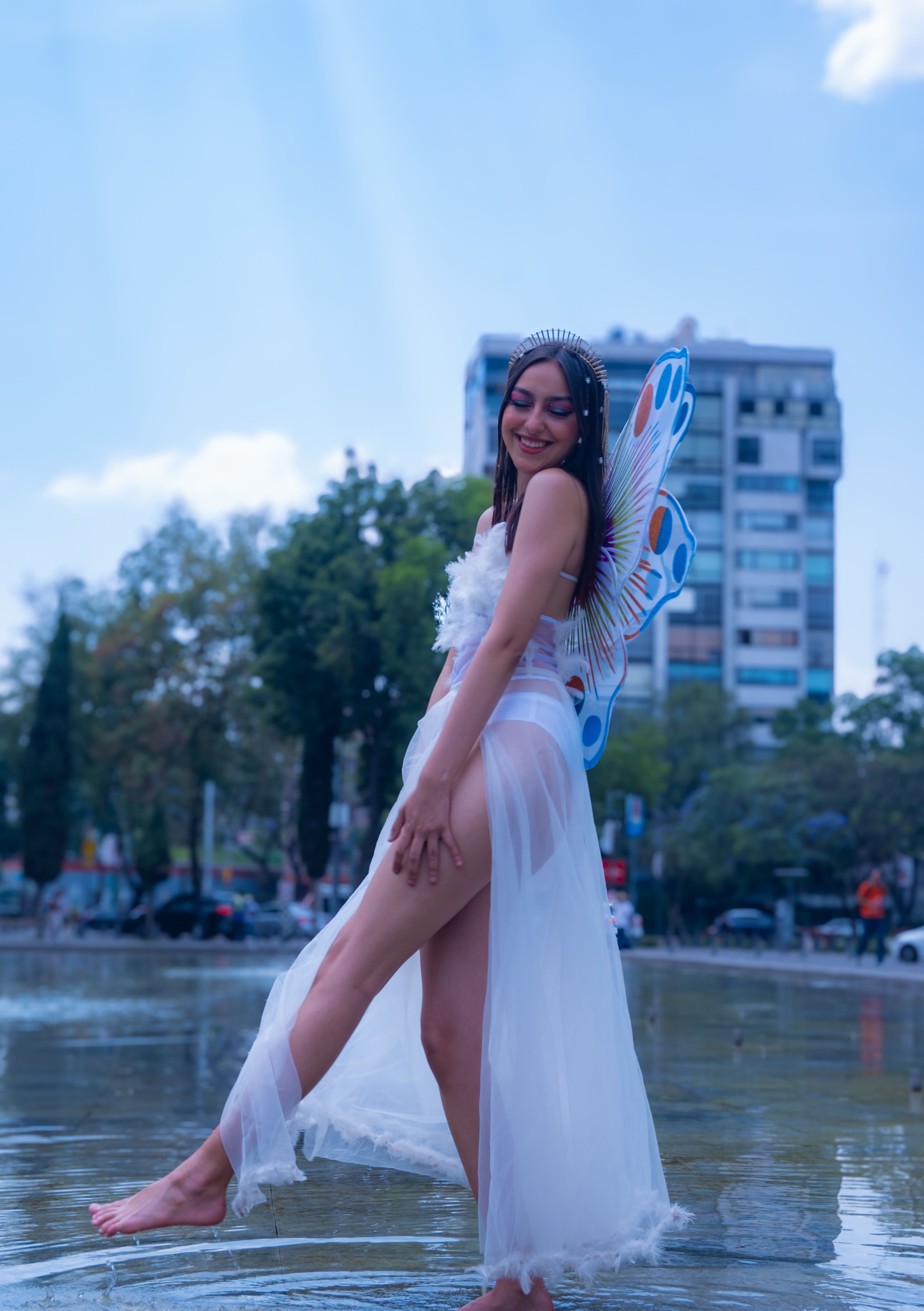 Fotomural Mujer sonriente con alas de mariposa posa en un vestido blanco al aire libre en Ciudad de México.