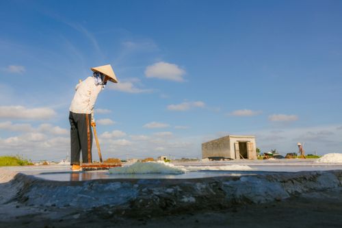 Free A farmer with a conical hat laboring in a rural salt field under a bright blue sky. Stock Photo