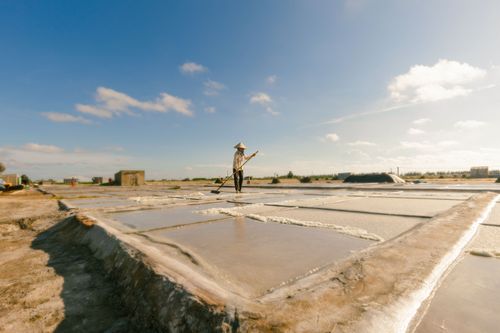 Free A farmer in Vietnam harvesting salt in bright sunlight wearing a conical hat. Stock Photo