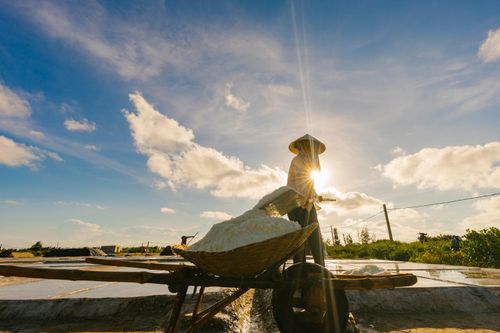 Free Silhouetted salt farmer with traditional hat works under a sunny sky, emphasizing rural lifestyle. Stock Photo
