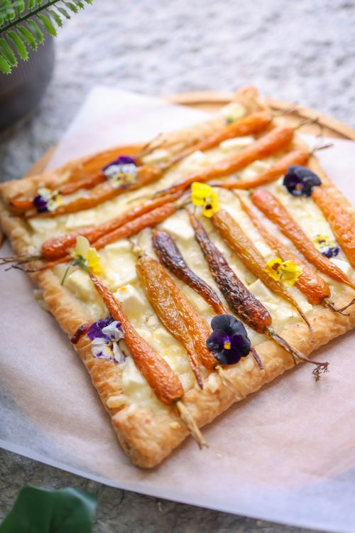 Free A close-up of a colorful vegetable tart adorned with carrots and edible flowers, showcasing food artistry. Stock Photo