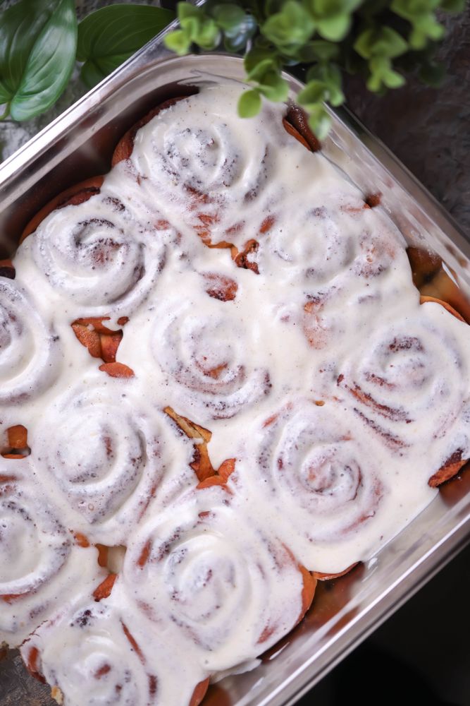 Rectangular metal pan filled edge to edge with tall golden cinnamon rolls covered generously in white vanilla cream cheese frosting