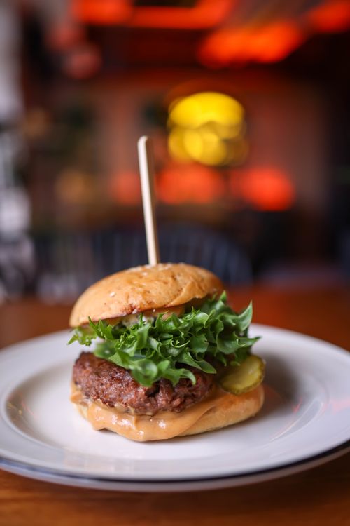 Free Close-up of a delicious gourmet burger with fresh lettuce and pickles on a white plate indoors. Stock Photo