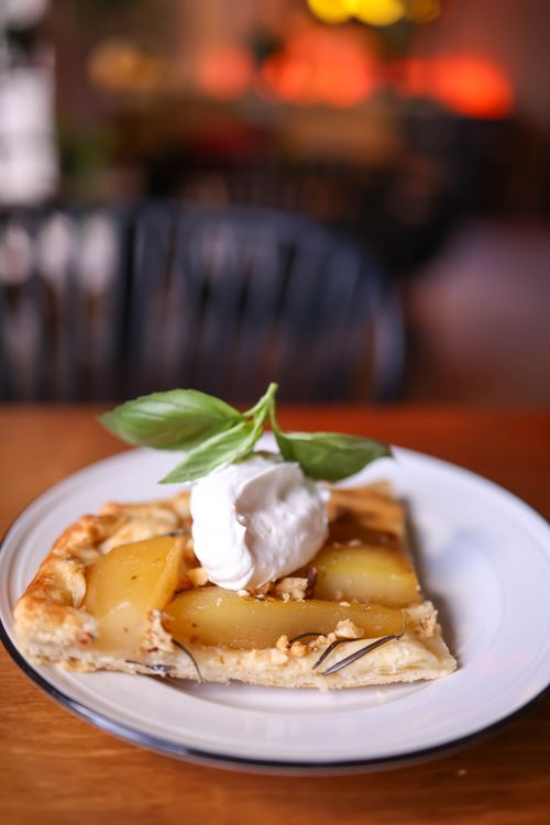 Free Close-up of an apple tart slice topped with whipped cream and basil leaves, perfect for dessert lovers. Stock Photo