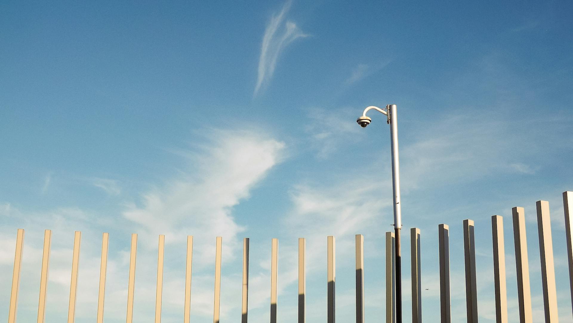 A surveillance camera mounted on a pole under a clear blue sky, capturing urban security essence.