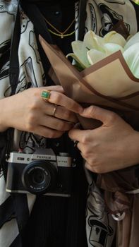 Close-up of elegant hands holding white flowers and camera with stylish scarf. Perfect for lifestyle and fashion themes.