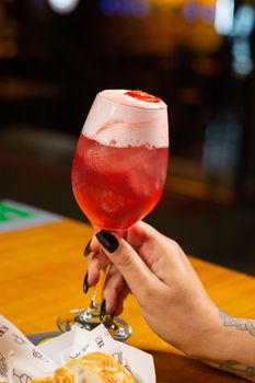 Close-up of a hand holding a vibrant red cocktail, showcasing detail and color.