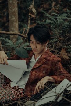 An Asian man in vintage attire reading bond papers in a forest setting.