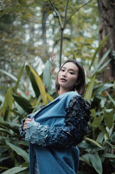 一位身着蓝色服装的时尚年轻女子在郁郁葱葱的森林绿植中摆姿势