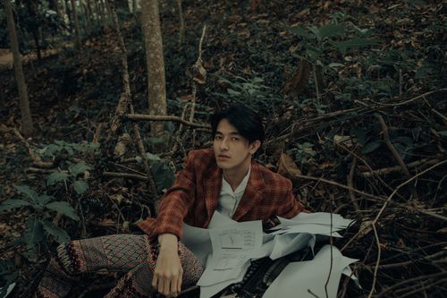Free Young man in plaid blazer with papers, exploring a forested area. Stock Photo