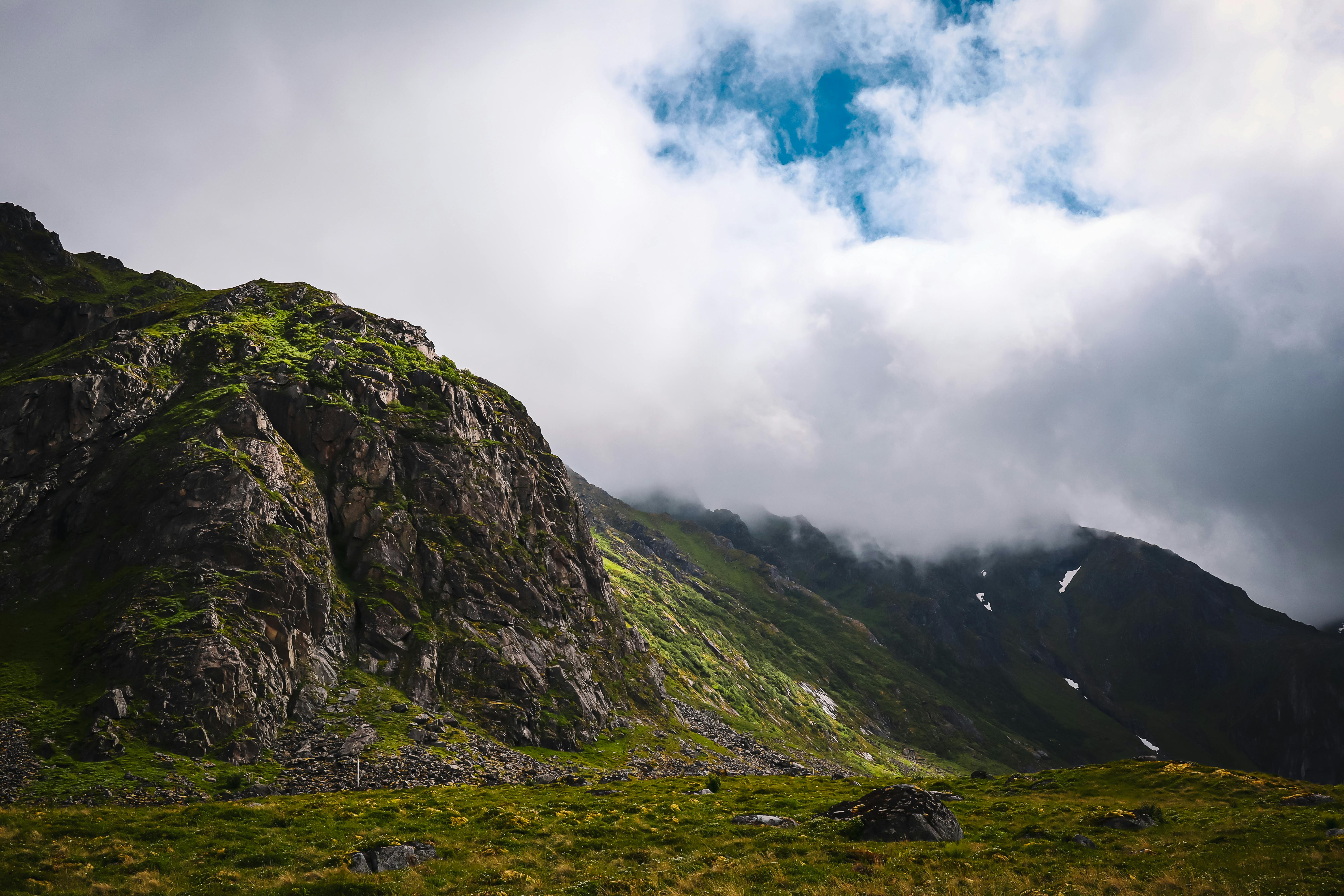 A mountain with grass and clouds in the sky