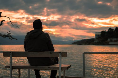 Free Silhouette of a person on a bench by a lake, watching a vibrant sunset. Stock Photo
