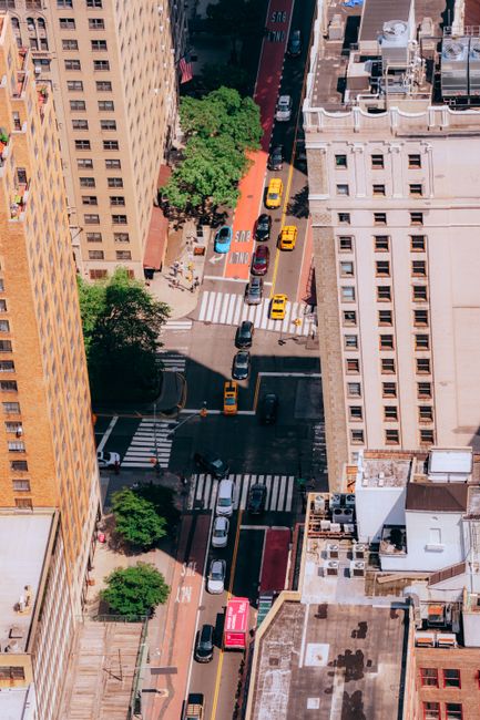 Bird's eye view of a busy New York City street intersection with traffic and towering buildings.
