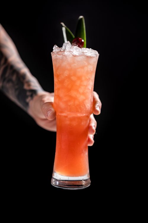 Free Vibrant fruity cocktail with ice and cherry garnish held against dark background. Stock Photo