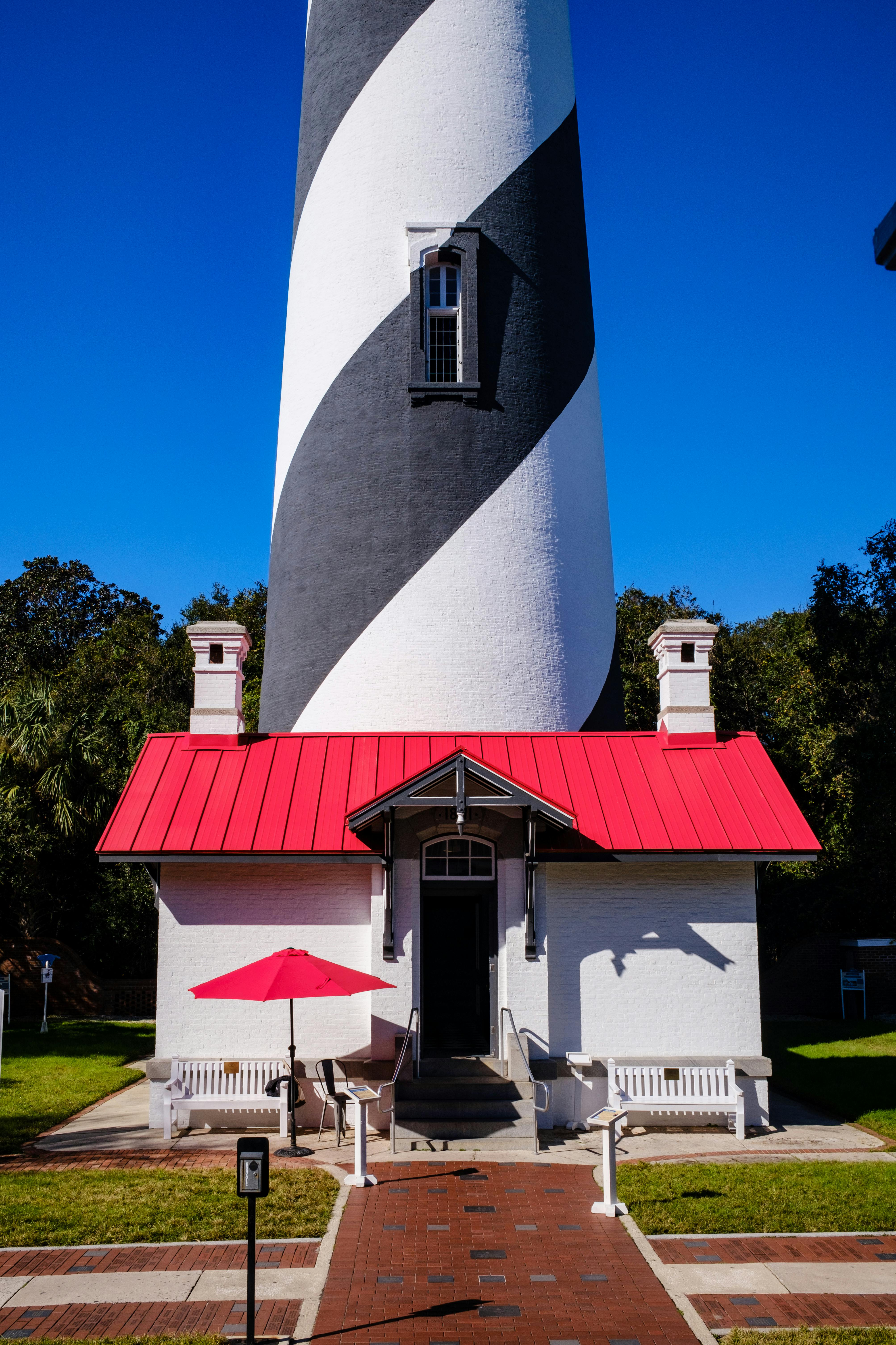 a white and red striped lighthouse with a red umbrella