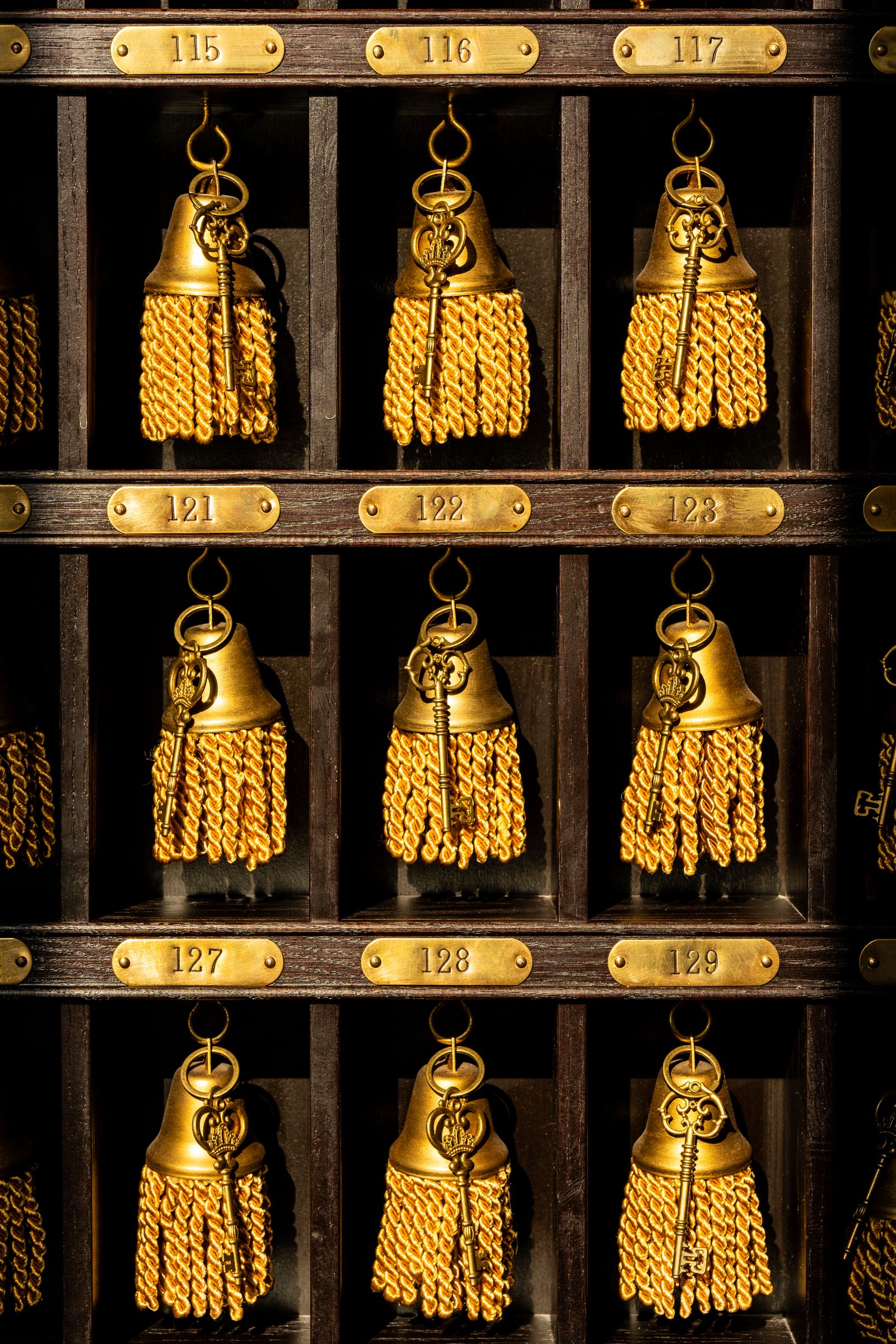 Close rack of brass room keys on numbered hooks behind a hotel counter