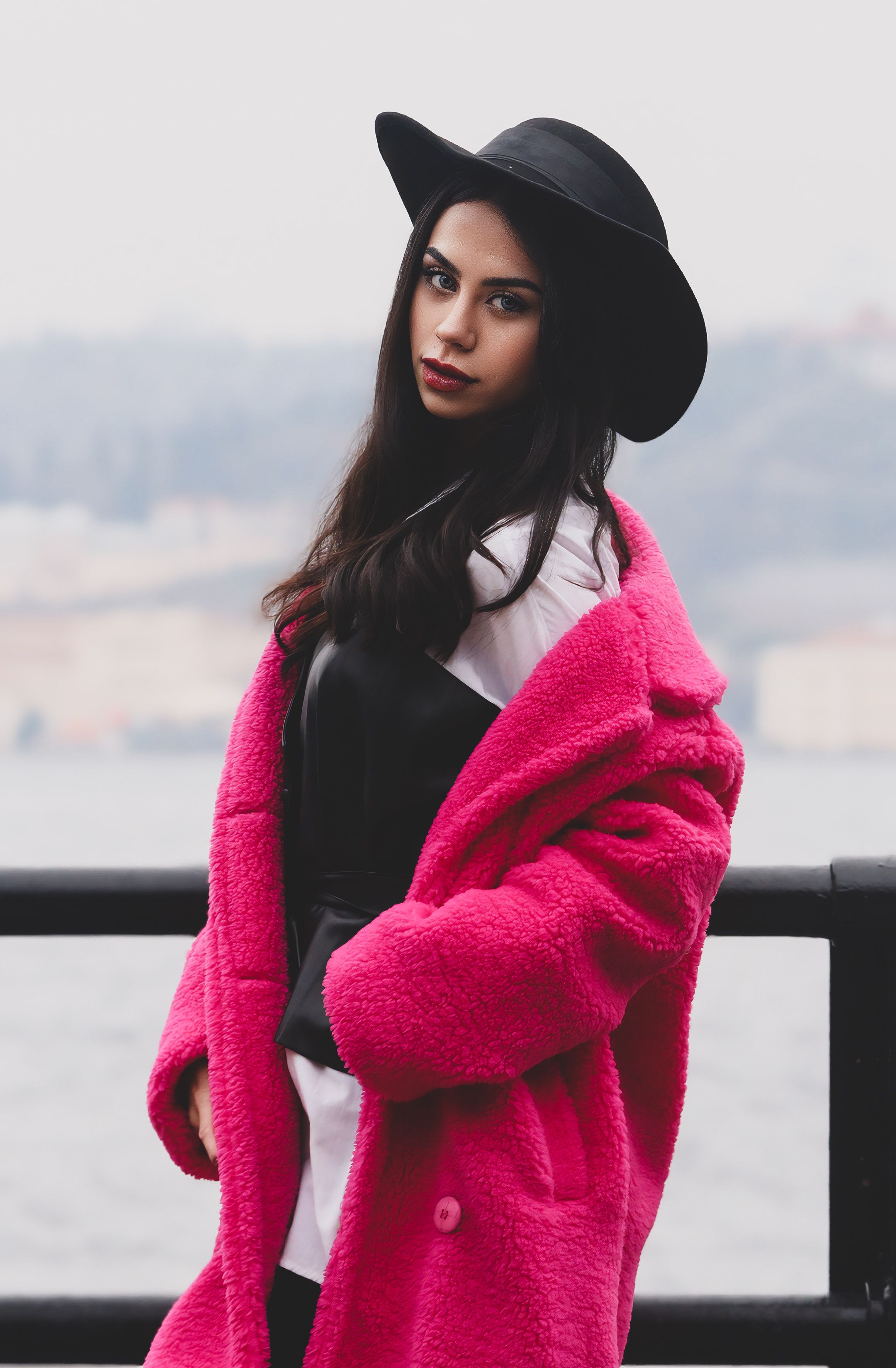 Fashionable woman in a pink coat posing by the shore in an urban setting.