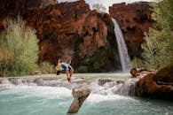 背景是雄伟的瀑布，一个人在溪流上进行后空翻，捕捉到冒险的本质