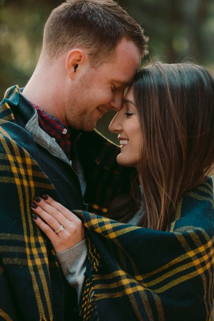 A couple wrapped in a plaid blanket sharing a tender moment in the fall season.