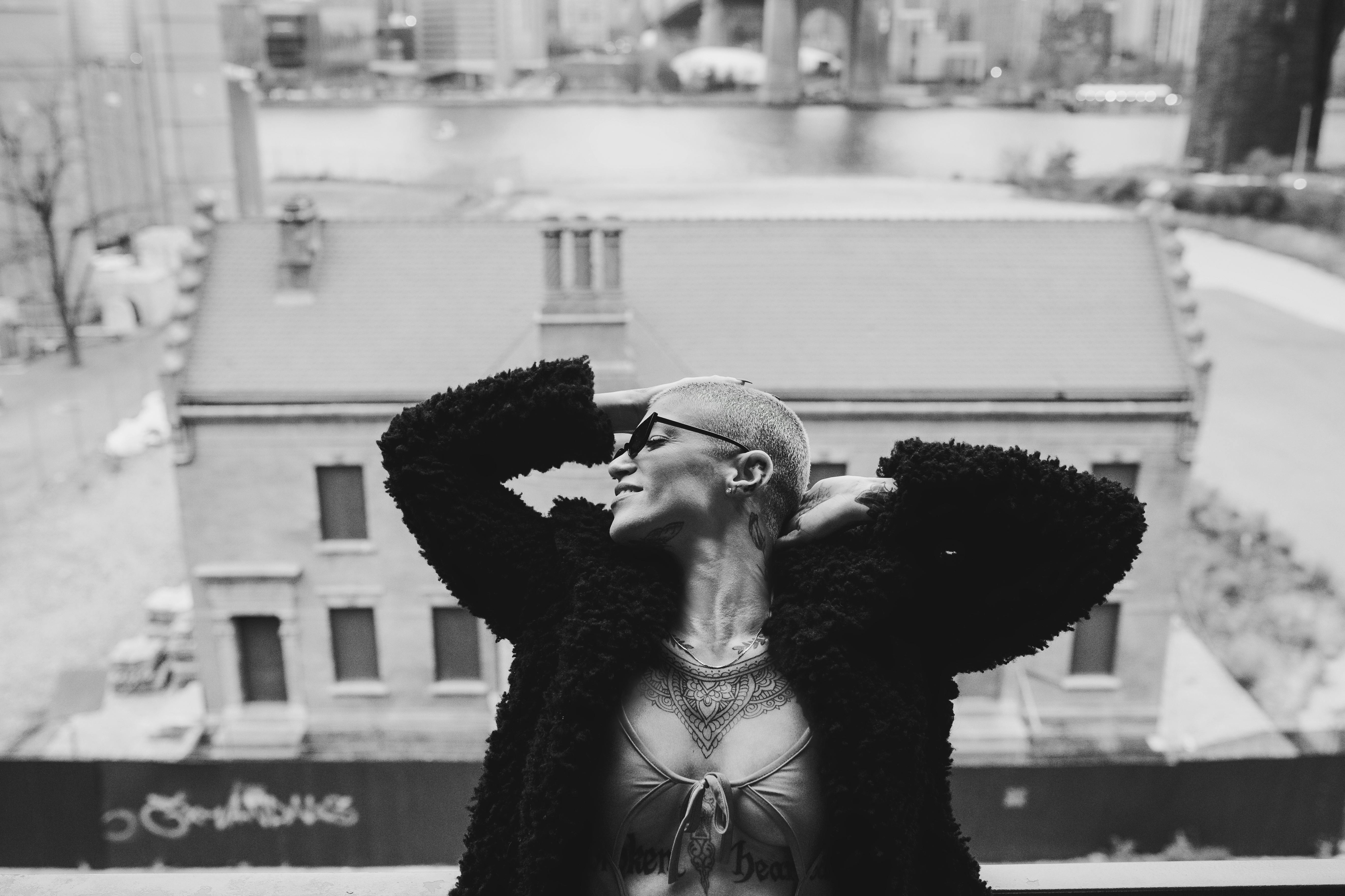 Black and white portrait of a stylish woman in sunglasses with a cityscape backdrop.
