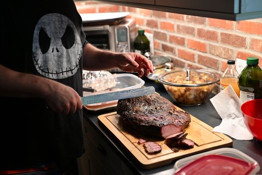 A person slices roast beef on a cutting board in a modern kitchen setting.