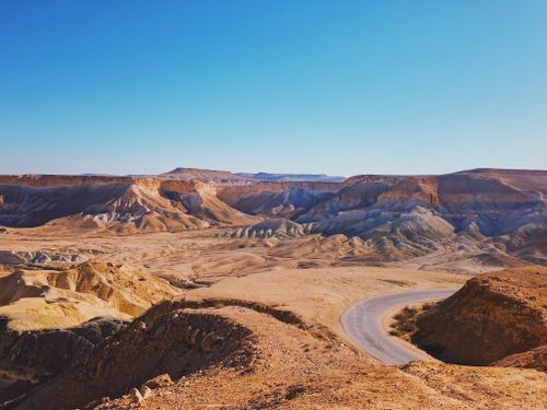 Free Explore the mesmerizing arid desert landscape featuring a winding road under a clear blue sky. Stock Photo