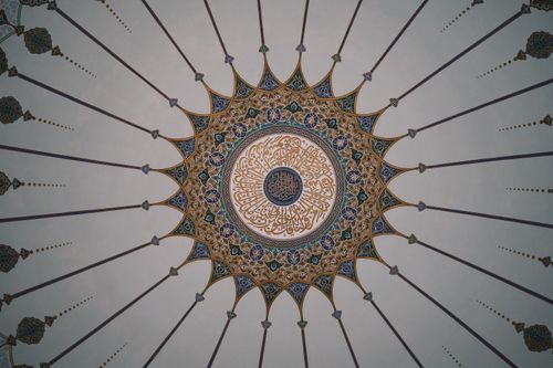 Free Detailed view of an ornate mosque dome ceiling featuring Islamic geometric and calligraphic designs. Stock Photo