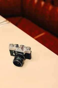 A classic vintage film camera resting on a light wooden table with a retro background.