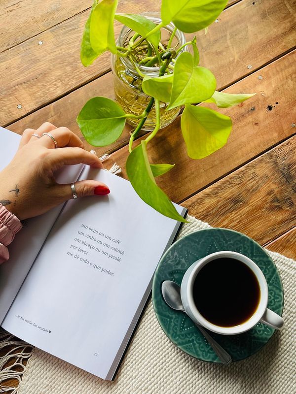 Livro aberto e xícara de café numa mesa de madeira, com planta ao lado