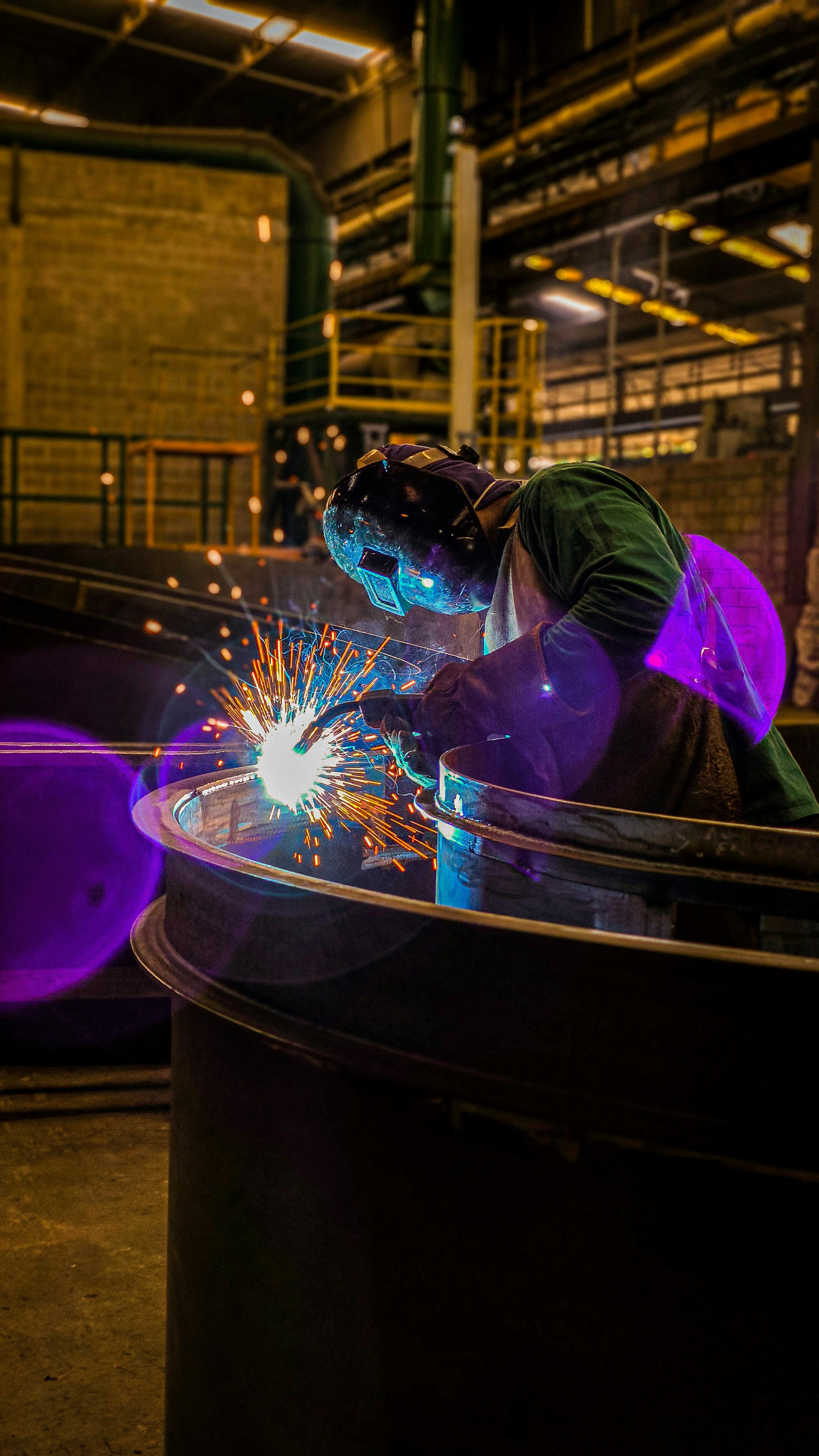 A skilled welder working with intense sparks in a dimly lit factory setting.