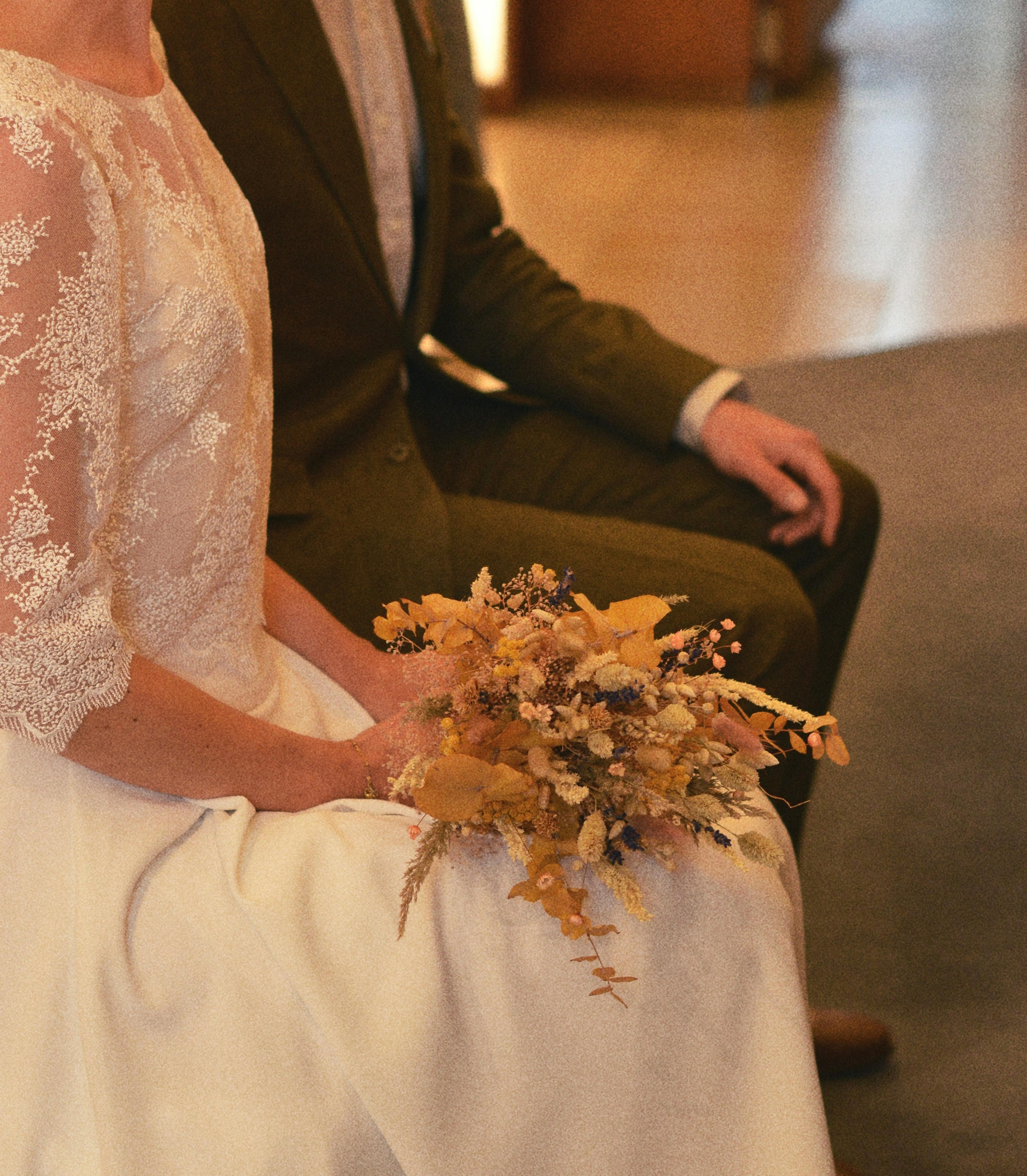 A close-up of a bride holding a bouquet, sitting beside the groom during a wedding ceremony.