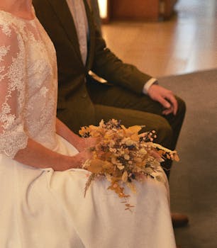 A close-up of a bride holding a bouquet, sitting beside the groom during a wedding ceremony.