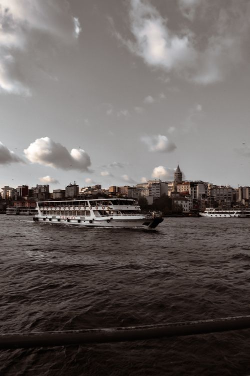 Free A picturesque ferry sailing near the iconic Galata Tower, under a cloudy Istanbul sky. Stock Photo