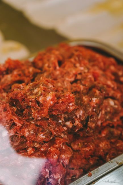 A mound of raw ground beef mince in a white bowl, showing its coarse, loosely packed texture and deep red color flecked with fat.