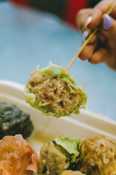 Close-up of a hand holding a colorful dumpling with chopsticks in Kuala Lumpur.