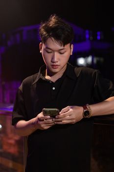 Portrait of a man using a smartphone at night with urban lights in the background.