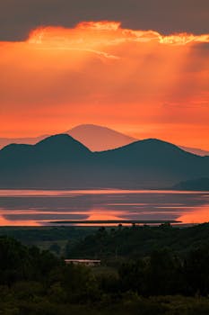 A breathtaking sunset with a silhouette of hills and reflective coastal waters.